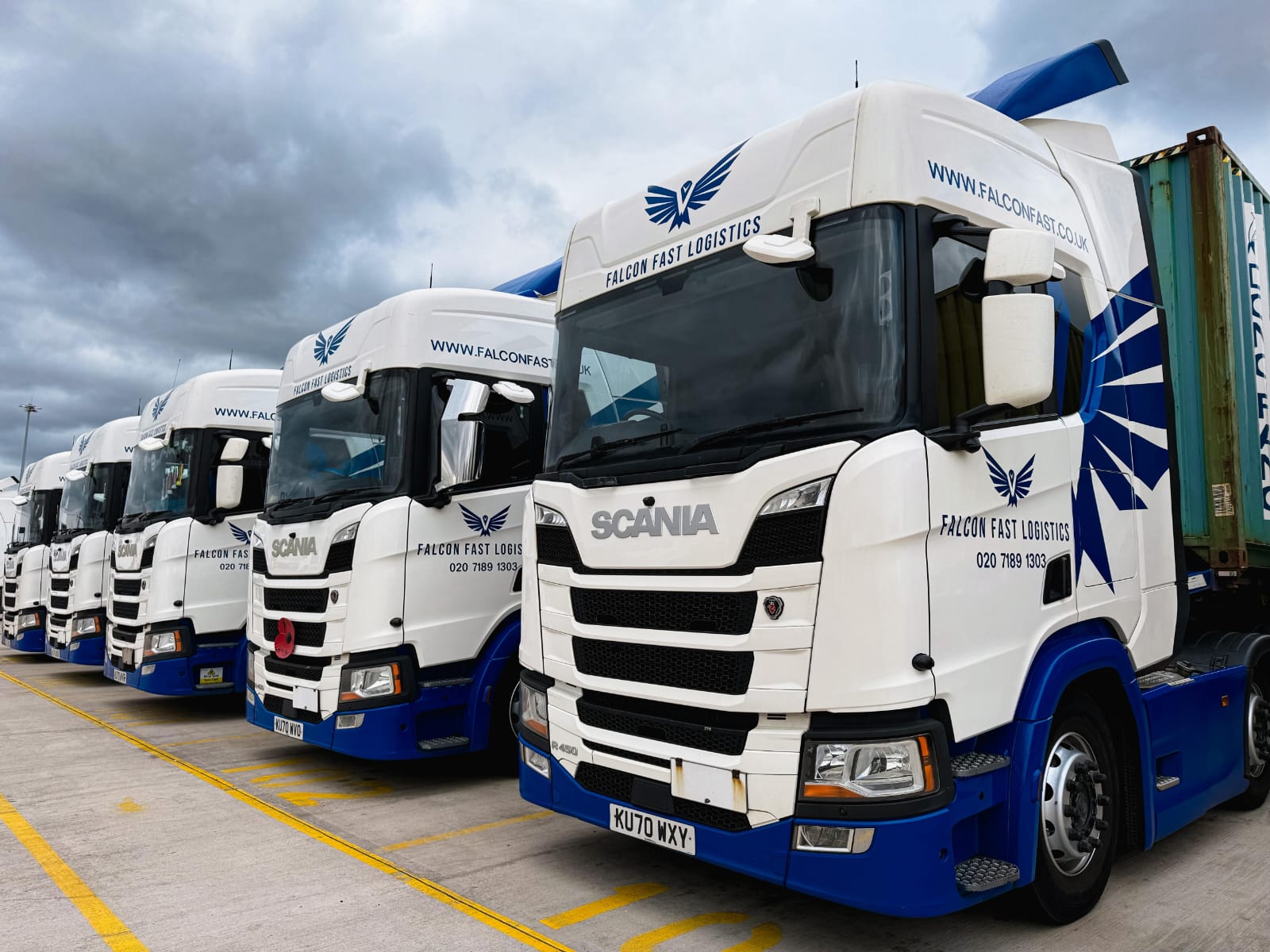 Row of Falcon Fast Logistics Scanias with a container on a moody day